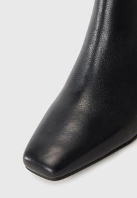 Black leather ankle boot with a pointed toe and smooth texture, featuring a sleek design and minimal hardware accents.