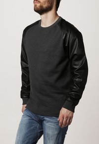 Sudadera gris oscuro con mangas de cuero negro, escote redondo, puños y dobladillo acanalados. Corte casual con un contraste de texturas entre las telas.