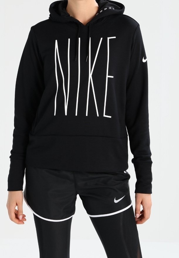 Personne portant un sweat à capuche Nike noir avec un grand logo blanc, un short Nike noir et des leggings noirs sur un fond clair uni.