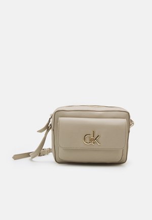 Borsa a tracolla in pelle beige con tasca anteriore a pattina, logo "ck" dorato e tracolla regolabile su sfondo bianco semplice.