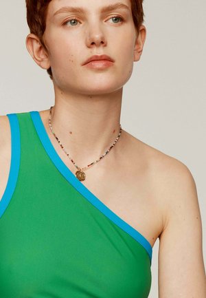Top verde de un solo hombro con ribete azul, hecho de una tela suave. Se lleva con un collar de cuentas multicolor que presenta un encanto dorado.