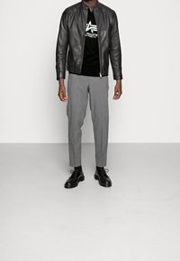 Černá kožená bunda, černé tričko s logem, šedé kalhoty na míru, černé šněrovací boty. Hladké textury, přiléhavý střih, monochromatické barvy.