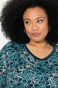 V-kaulustoppi tumman teallin värissä, jossa on kukkakuvio, sisältäen turkoosin ja valkoisen sävyjä, sekä pehmeä, teksturoitu kangas.