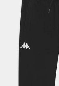 Zwarte broek met zijzak en een wit logo van twee rug aan rug zittende figuren nabij de zak.