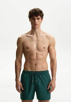 Costumi da bagno verdi realizzati in materiale leggero, con vita elasticizzata e cordino. Il design è semplice e privo di motivi.