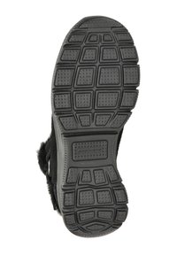 Zapatilla negra con una suela de goma texturizada que presenta un patrón de cuadrícula y pequeños puntos elevados. Acentos de suave peluche en el lateral.