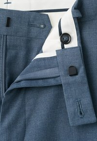 Detailné zábery na pás modrých nohavíc od obleku, zobrazujúce zips, gombík, háčik so závesom a bielu vnútornú podšívku s detailom námorníckej modrej lemovky.