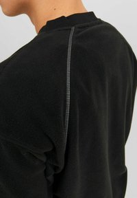 Čierna fleecová mikina s textúrovaným povrchom, rebrovaným golierom a kontrastným šitím podél švov.