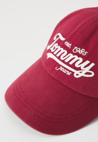 Punainen puuvillainen baseball-lippalakki, jossa valkoinen brodeerattu "Tommy Jeans" -teksti ja perustamisvuosi, kaareva lippa ja teksturoitu kangas.