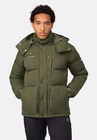 Grøn dynejakke med høj krave, flere lommer og knaplukninger. Har et tekstureret stof og justerbar snøre til hætten.