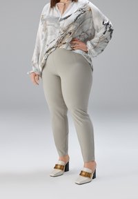 Losse zijden blouse in wit met grijze en gouden marmerpatronen, gecombineerd met nauwsluitende lichtgrijze broek en witte mules met blokhak en gouden accenten.