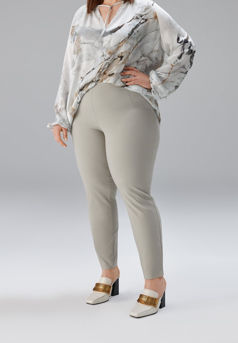 Losse zijden blouse in wit met grijze en gouden marmerpatronen, gecombineerd met nauwsluitende lichtgrijze broek en witte mules met blokhak en gouden accenten.