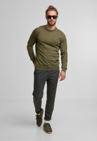 Suéter de punto verde oliva con cuello redondo, combinado con pantalones jogger ajustados gris oscuro y zapatos casuales marrones.