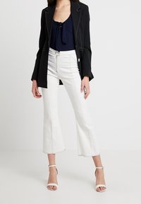 Svart kavaj med vit söm, marinblå ribbad topp med rosettdetalj, vita korta utsvängda byxor och vita klackar med ankelrem.