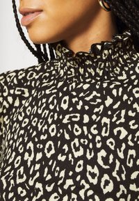 Tessuto nero con stampa leopardata beige, caratterizzato da un alto colletto arricciato. Il materiale appare textured e morbido, evidenziando il motivo distinto.