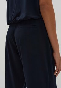 Marineblauwe broeken met een losse pasvorm, met een gladde textuur, een subtiele achterzak en een hoog model. Zachte stof valt elegant.