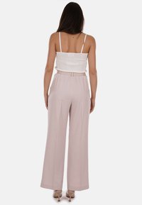 Pantaloni a vita alta e gamba larga in morbido tessuto rosa con elastico in vita; abbinati a un top canotta bianco aderente.