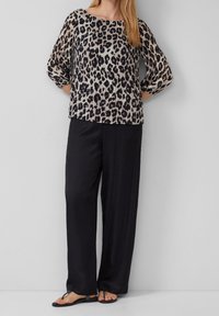 Blouse plissée à imprimé léopard avec un pantalon noir à jambes larges. Le haut présente un col bateau et des manches trois-quarts ; tissu léger.