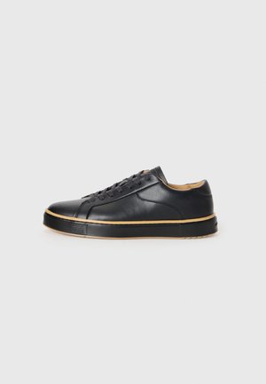 Schwarze Leder-Sneaker mit runder Zehenpartie, einfarbigen Schnürsenkeln, einer strukturierten Gummisohle und einem kontrastierenden beigen Rand, ausgestattet mit einer glatten Oberfläche.