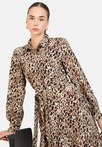 Robe chemise en satin à motif léopard, avec un col, des manches longues, une taille ceinturée et une silhouette fluide avec une finition brillante.