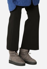 Botas de tobillo grises acolchadas con suelas de goma negras, que cuentan con un cierre de cordón y una textura suave y acolchada. Combinadas con pantalones de campana negros.
