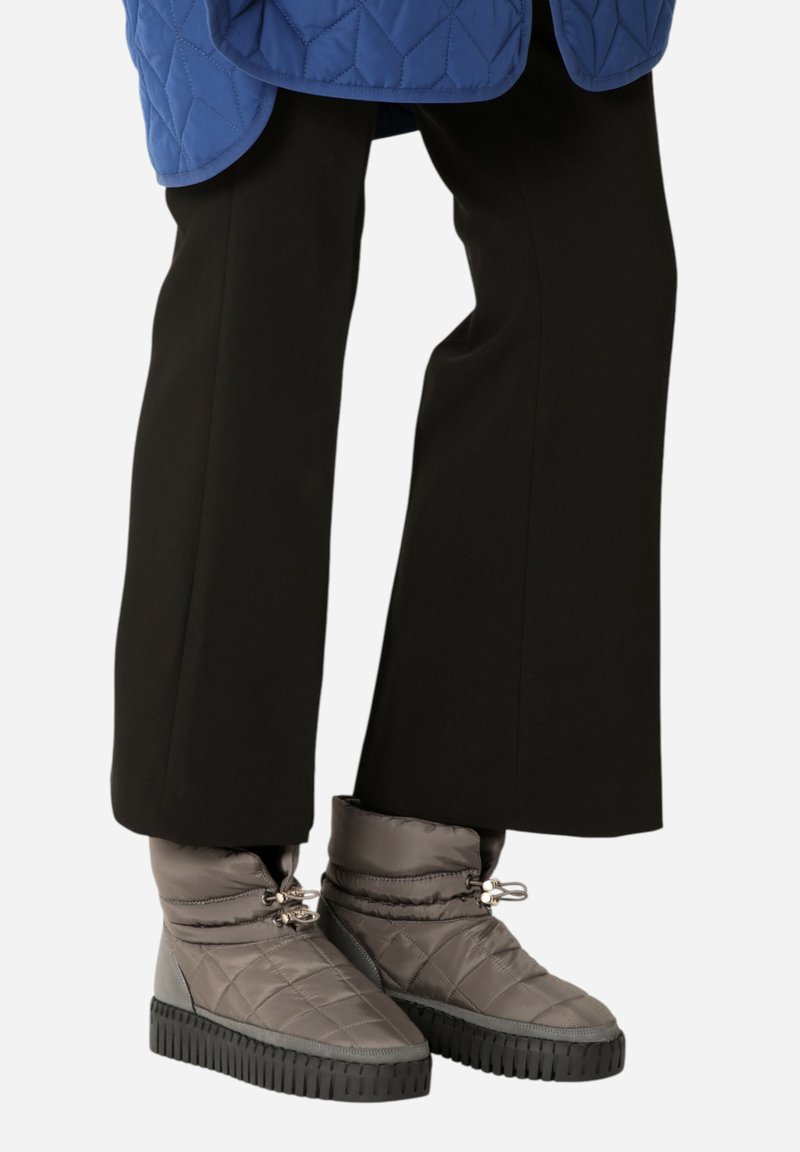 Botas de tobillo grises acolchadas con suelas de goma negras, que cuentan con un cierre de cordón y una textura suave y acolchada. Combinadas con pantalones de campana negros.