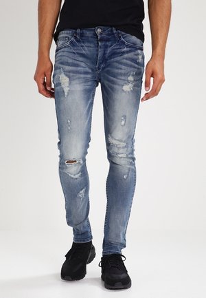 Blå denimjeans med slim fit, som har slitna lappar och whiskering-effekter. Tyget har en något blekt finish.