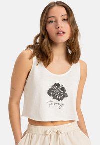 White crop top made of lightweight fabric, featuring a black floral graphic and "Roxy" text at the bottom. Round neckline, sleeveless design.