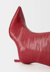 Red faux-crocodile leather ankle boot with a pointed toe, slim heel, and a smooth, glossy finish. The design features a textured pattern.