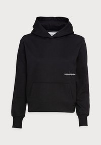 Sudadera de algodón negra con un bolsillo frontal, puños acanalados y capucha con cordón. Presenta un logotipo bordado de "CALVIN KLEIN JEANS" en el pecho.