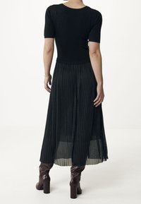 Černý úzký top s krátkým rukávem v kombinaci s plisovanou černou sukní, doplněný o vysoké bordó boty do kolen a textura látky.