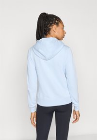 Φωτεινή γαλάζια μπλούζα με κουκούλα από μαλακό ύφασμα, με μεγάλη κουκούλα, ριμπ μανσέτες και εφαρμοστή μέση, φορεμένη πάνω από μαύρο κολάν.