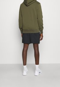 Haut à capuche vert olive avec un cordon de serrage, assorti à un short sombre et des baskets blanches avec des accents bleus. Texture de tissu lisse.