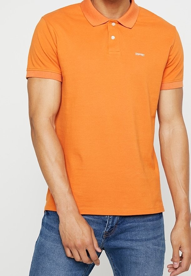 Polo arancione a maniche corte in cotone, con colletto classico e un logo discreto sul petto, abbinato a jeans in denim.