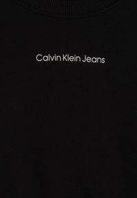 Sudadera negra con cuello redondo acanalado y logotipo "Calvin Klein Jeans" en blanco, centrado en la parte frontal con una tipografía moderna.