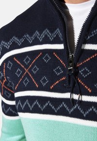 Gestrickter Pullover mit halbhohem Reißverschluss. Er verfügt über einen marineblauen Körper, weiße und türkisfarbene Streifen sowie geometrische Muster in Orange und Grau.