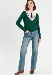 Grøn striktrøje med V-hals og hvide og gule striber, parret med lys blå lige ben jeans og brune hælede ankelstøvler.