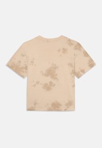 Beżowa koszulka z krótkim rękawem w wzór tie-dye w brązowym kolorze. Wykonana z miękkiej bawełny, ma okrągły dekolt i prosty dół.