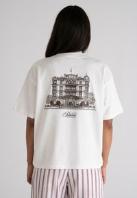 White cotton t-shirt featuring a black illustration of a grand building on the back, with "Prohibited Grand Resort" text below.