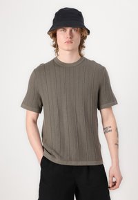 Olivengrøn strikket kortærmet sweater med teksturerede lodrette striber, rund halsudskæring og ribbede manchetter. Bæret med sorte shorts.