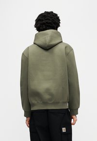 Olivgrüner Hoodie mit Kordelzugkapuze, gerippten Bündchen und Saum. Verfügt über eine weiche Textur und eine lockere Passform, kombiniert mit schwarzen Cargohosen.