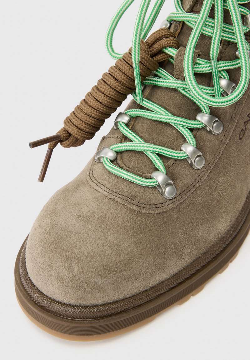 Brauner Wildleder-Wanderschuh mit grünen und braunen Schnürsenkeln, Metallösen und einer abgerundeten Zehenpartie. Verfügt über eine robuste Gummisohle für guten Halt.