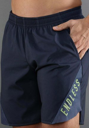 Hombre que lleva pantalones cortos deportivos azul marino con cintura elástica y la palabra "ENDLESS" impresa en el área del bolsillo lateral.