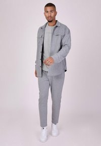 Lys grå skjorte med knaplukning over en grå T-shirt, parret med matchende grå bukser og hvide sneakers; glat stof og enkelt design.
