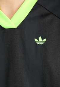 Svart idrottströja med grön V-ringning, subtila vertikala ränder och en liten grön Adidas-logga på vänster bröst.