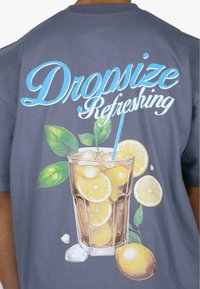 Grå t-shirt med et farverigt grafik af en drink i et klart glas med citronskiver og mynteblade, samt teksten "Dropsize Refreshing."