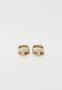 Mules en plastique beige avec un petit talon épais. Texture lisse avec des bords arrondis et un dos prononcé. Logo "TOMMYJEANS" subtilement embossé.