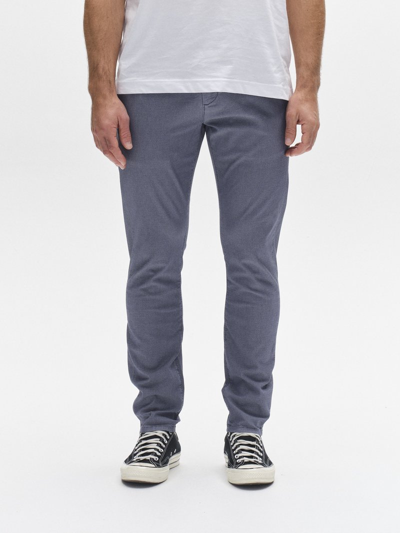 Lahke, temno modre bombažne hlače s tesnim krojem in subtilno teksturo, kombinirane s črnimi platnenimi supergami z belimi podplati in vezalkami.