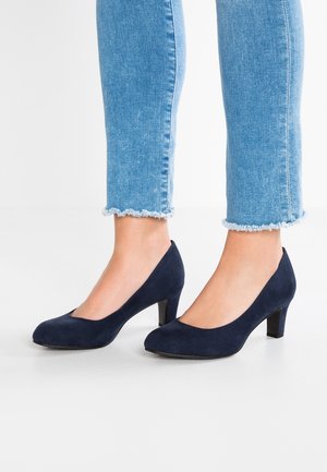 Navy blue suede heels with a rounded toe and a small, chunky heel; paired with light blue frayed hem jeans.
