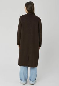 Manteau marron en mélange de laine avec une coupe droite, manches longues, et une fente au dos. Associé à un jean large en denim bleu clair.